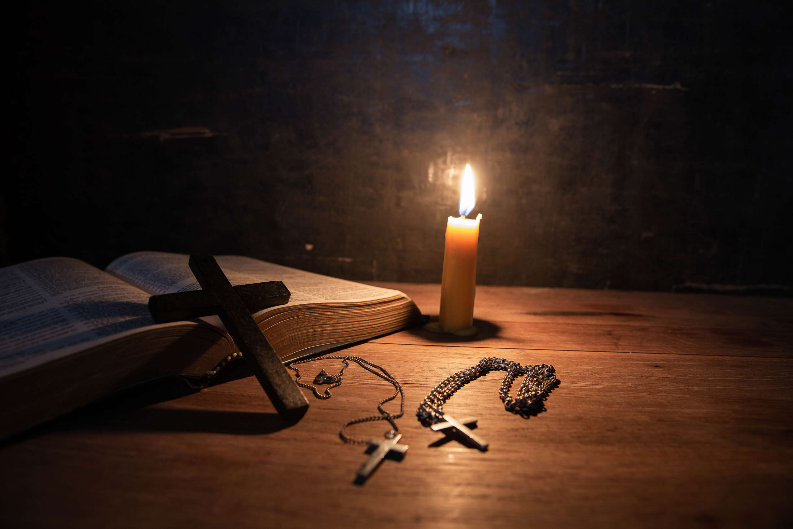 Cross with bible and candle on a old oak wooden table. Beautiful gold background. Religion concept.
